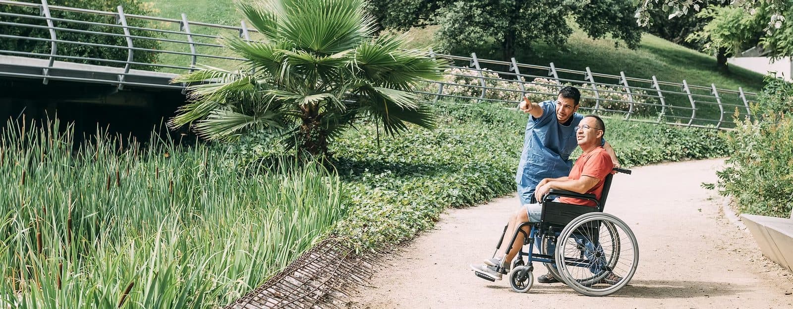 Man in a wheelchair and a companion on an outdoor park path