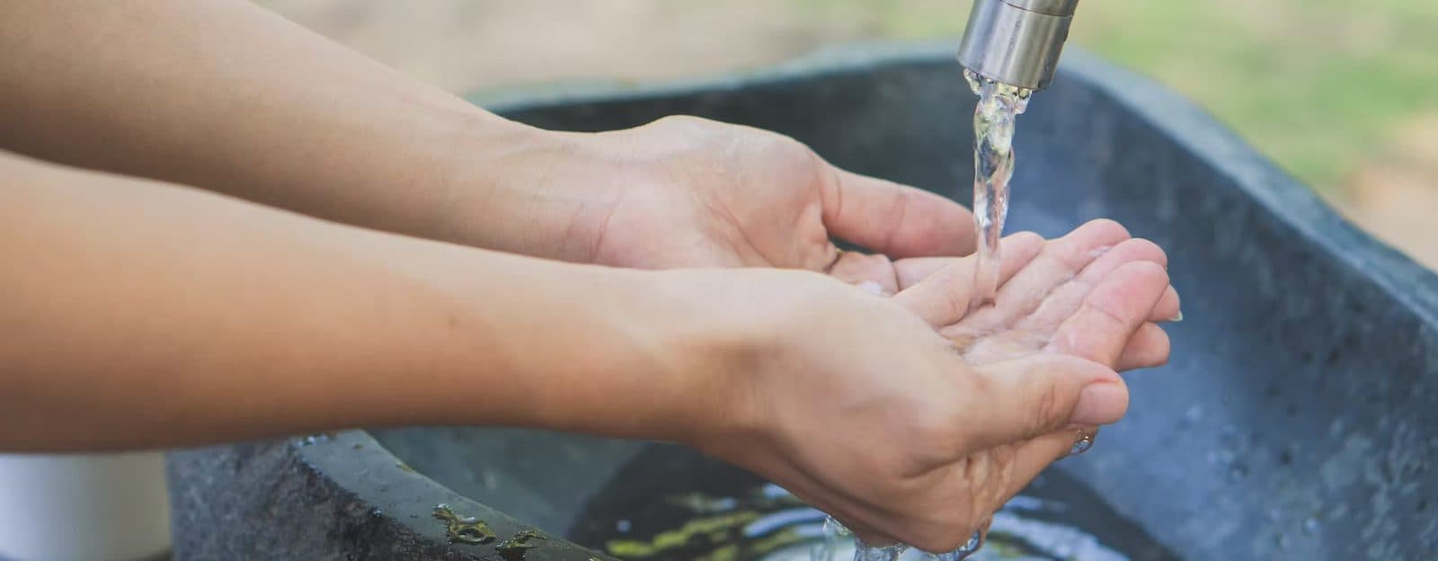 Hands being washed under an outdoor faucet